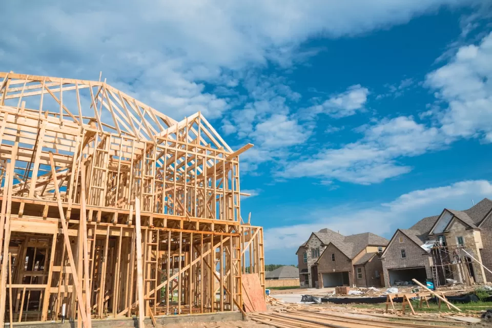 Wood-framed houses under construction with brick-covered completed homes in background.